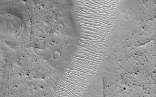 <h1>PIA04734:  Arabia's Auqakuh Vallis</h1><div class="PIA04734" lang="en" style="width:603px;text-align:left;margin:auto;background-color:#000;padding:10px;max-height:150px;overflow:auto;">MGS MOC Release No. MOC2-477, 8 September 2003<p />This Mars Global Surveyor (MGS) Mars Orbiter Camera (MOC) image shows a portion of southern Auqakuh Vallis in northeastern Arabia Terra. The floor of this ancient valley--which might have been carved by a liquid such as water--is today covered by large, windblown, ripple-like bedforms. The terrain surrounding the valley has been eroded such that only remnants of former craters and layered bedrock remain. The valley was once much deeper, but material of hundreds, if not thousands, of meters thickness has been removed. This picture is located near 28.9°N, 299.9°W; it covers an area 3 km (1.9 mi) across and is illuminated by sunlight from the lower left.<br /><br /><a href="http://photojournal.jpl.nasa.gov/catalog/PIA04734" onclick="window.open(this.href); return false;" title="Voir l'image 	 PIA04734:  Arabia's Auqakuh Vallis	  sur le site de la NASA">Voir l'image 	 PIA04734:  Arabia's Auqakuh Vallis	  sur le site de la NASA.</a></div>