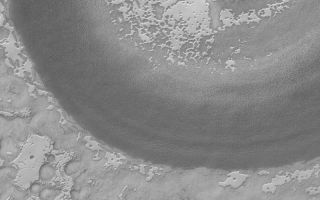 <h1>PIA05281:  Exhuming South Polar Crater</h1><div class="PIA05281" lang="en" style="width:800px;text-align:left;margin:auto;background-color:#000;padding:10px;max-height:150px;overflow:auto;">7 February 2004 <br /> The large, circular feature in this image is an old meteor impact crater. The crater is larger than the 3 kilometers-wide (1.9 miles-wide) Mars Global Surveyor (MGS) Mars Orbiter Camera (MOC) image, thus only part of the crater is seen. The bright mesas full of pits and holes--in some areas resembling swiss cheese--are composed of frozen carbon dioxide. In this summertime view, the mesa slopes and pit walls are darkened as sunlight causes some of the ice to sublime away. At one time in the past, the crater shown here may have been completely covered with carbon dioxide ice, but, over time, it has been exhumed as the ice sublimes a little bit more each summer. The crater is located near 86.8°S, 111.6°W. Sunlight illuminates this scene from the upper left.<br /><br /><a href="http://photojournal.jpl.nasa.gov/catalog/PIA05281" onclick="window.open(this.href); return false;" title="Voir l'image 	 PIA05281:  Exhuming South Polar Crater	  sur le site de la NASA">Voir l'image 	 PIA05281:  Exhuming South Polar Crater	  sur le site de la NASA.</a></div>